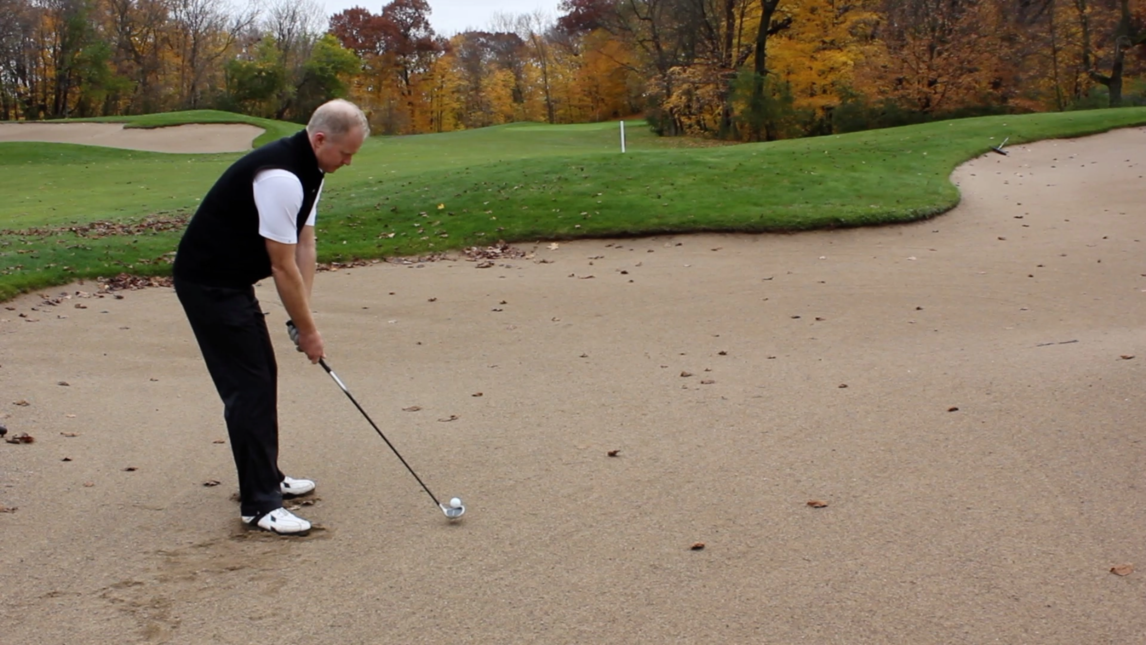 A golfer hits a ball from a sand bunker